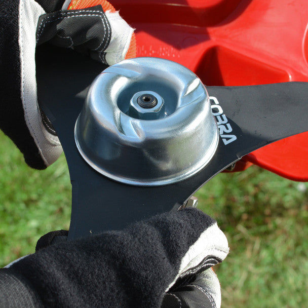 Close-up of a Cobra BC330CU blade held by gloved hands with a blurred grass background
