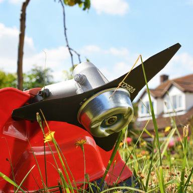 Cobra BC330CU grass strimmer large blade in grass, blurred house and trees in the background