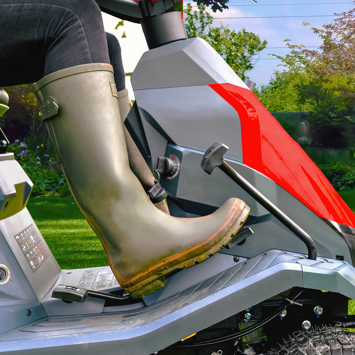 Person wearing Wellington boots operating the throttle of a Cobra LTX66HRL lawn mower with a garden background