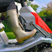 Person wearing Wellington boots operating the throttle of a Cobra LTX66HRL lawn mower with a garden background