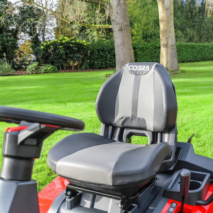 Gray and black seat with arm rests of a Cobra premiumride on  lawn tractor on a grassy area with trees in the background