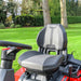Gray and black seat with arm rests of a Cobra premiumride on  lawn tractor on a grassy area with trees in the background