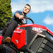 Man heroicly sitting on a red and black cobra premium lawn tractor with a clear blue sky and trees in the background