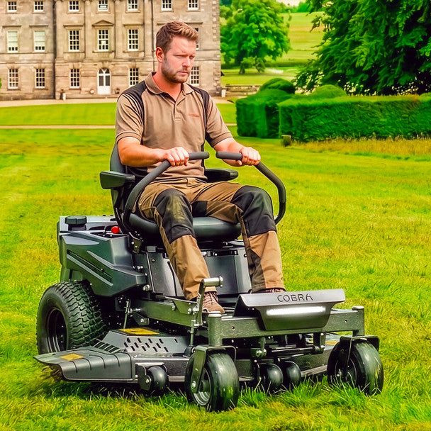 Man operating a Cobra ztr42l lawn mower in a large grassy area with a building in the background