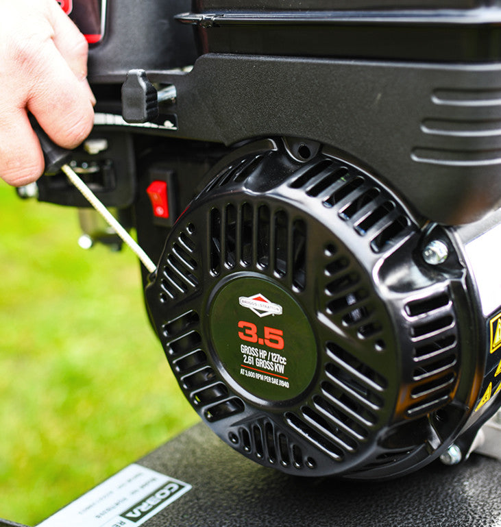 Close-up of a  briggs and straton being started via the pull cord starter. All against a grassy background.