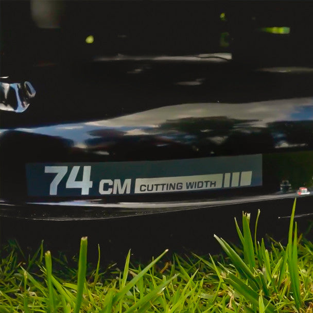 Close-up of a lawn mower deck with '74 CM CUTTING WIDTH' label on grass