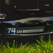 Close-up of a lawn mower deck with '74 CM CUTTING WIDTH' label on grass