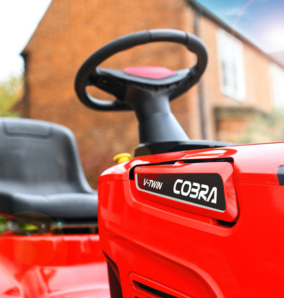 Red Cobra V-Twin ride-on lawn mower with steering wheel and seat in front of a brick building.