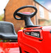 Red Cobra V-Twin ride-on lawn mower with steering wheel and seat in front of a brick building.