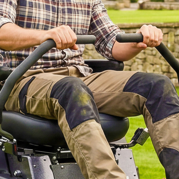 Person operating a a cobra zero turn lawn mower on a grassy area with a stone wall in the background.