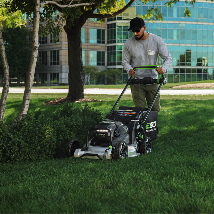 Man using an EGO lawn mower in a park with a building in the background