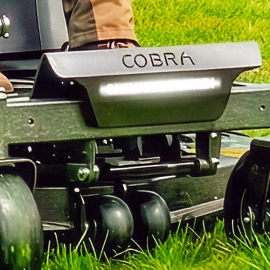 Close up of the front of a Cobra ZTR50L zero turn lawn mower with 'Cobra' branding next to LED headlights on a grassy background