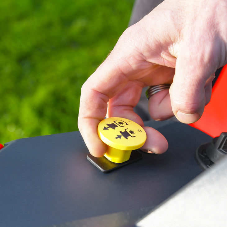 Hand pressing a yellow blade engagement button on a Cobra premium ride on lawn tractor with a green background
