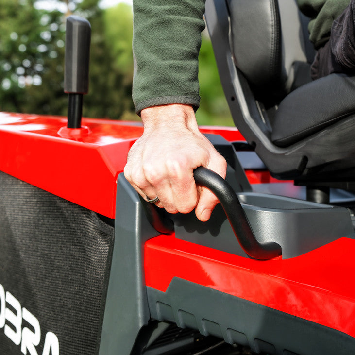 Hand adjusting the seat settings on a Cobra premium ride on lawn tractor, against a grassy background 
