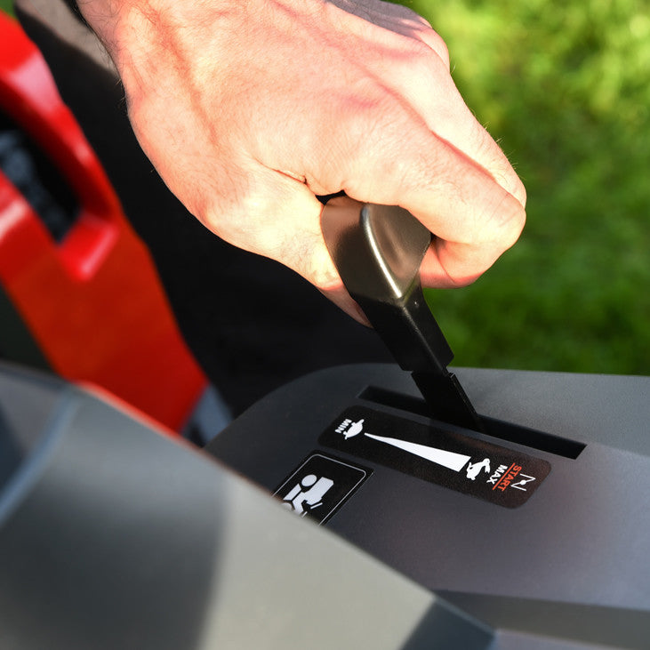 Hand using the throttle control on a cobra premium ride on lawn tractor, against a grassy background