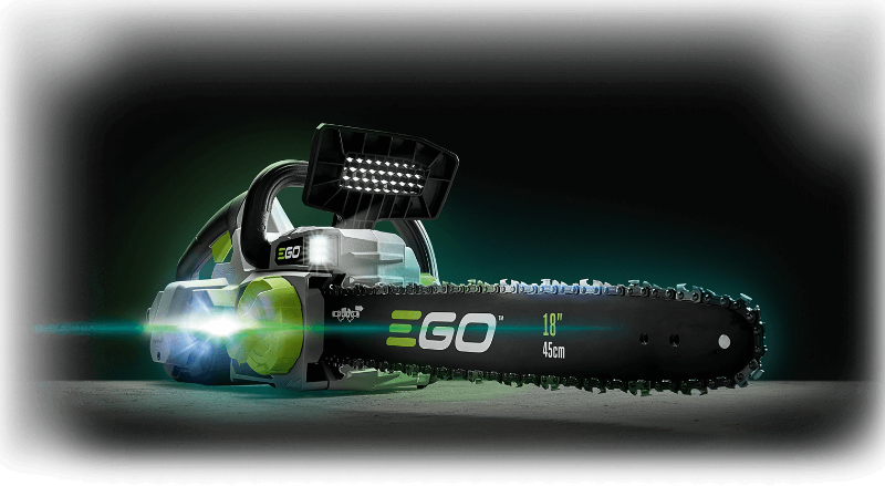A cordless chainsaw with integrated LED lights on the handle and front, shown in a dark studio-style setting with green glow effects. The bar and handle are black with bright green and white EGO branding.